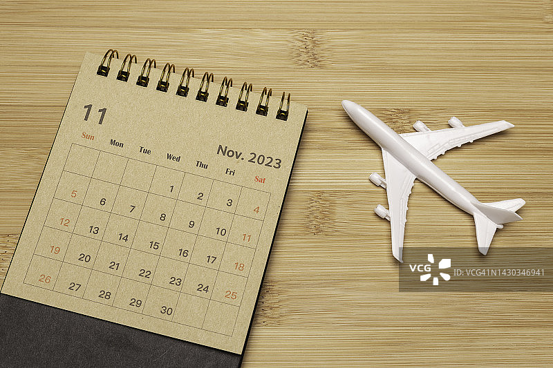 日历桌2023:11月是组织者计划和截止日期的月份，在木制背景下的飞机模型。旅行的概念。图片素材