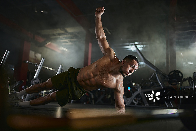 肌肉发达的男子在健身房单手平板支撑的姿势锻炼耐力。图片素材