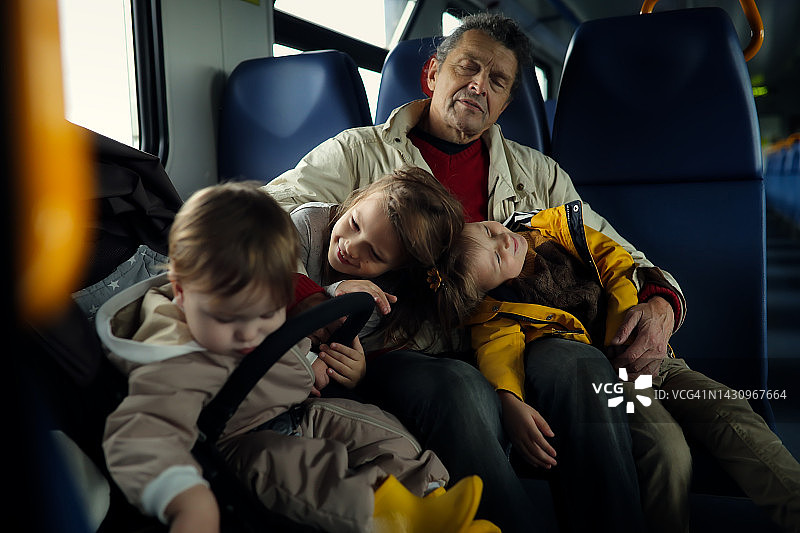 老人和他的孩子睡在电动火车上旅行。有三个孩子的男人。图片素材