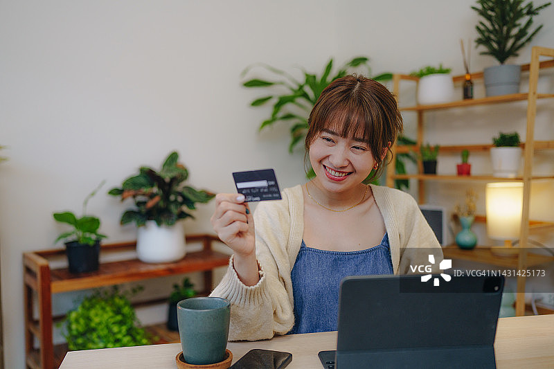 年轻的亚洲女性用平板电脑在网上购物，在家用信用卡进行移动支付图片素材