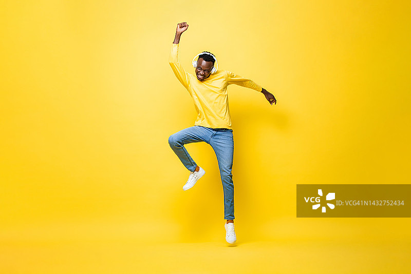欣喜若狂的年轻非洲人戴着耳机听音乐和跳舞的手在工作室黄色孤立的背景图片素材