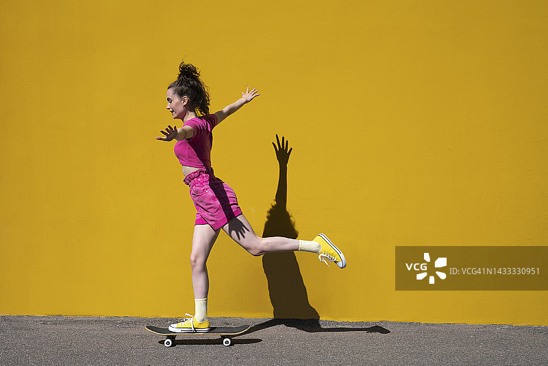 女子张开双臂，在墙前的滑板上保持平衡图片素材