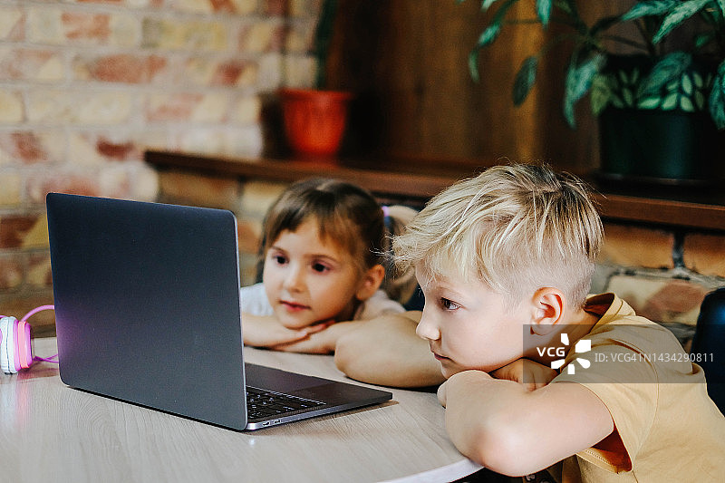 在线学习。孩子们坐在桌子旁，看着笔记本电脑的屏幕。哥哥和姐姐一起学习图片素材