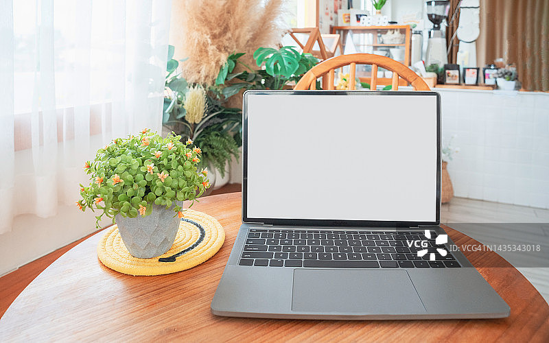 笔记本电脑空白屏幕在桌子上的咖啡馆背景。咖啡店桌子上黑屏的笔记本电脑模糊了背景图片素材