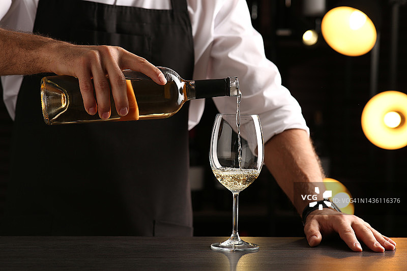 酒保将白葡萄酒倒入室内柜台的玻璃杯中，特写图片素材