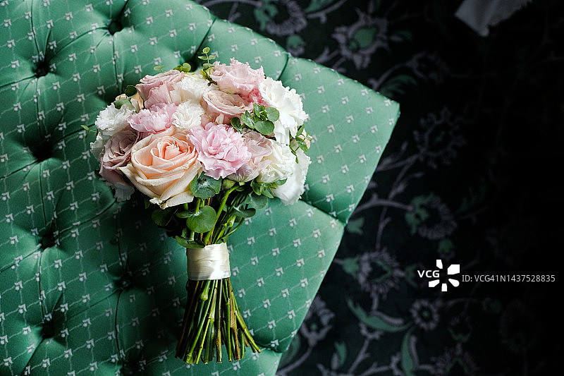 漂亮的婚礼花束放在豪华的天鹅绒椅子上，特写。花束不同的花朵和绿叶，用缎带系，模糊的背景。婚礼的主题。图片素材