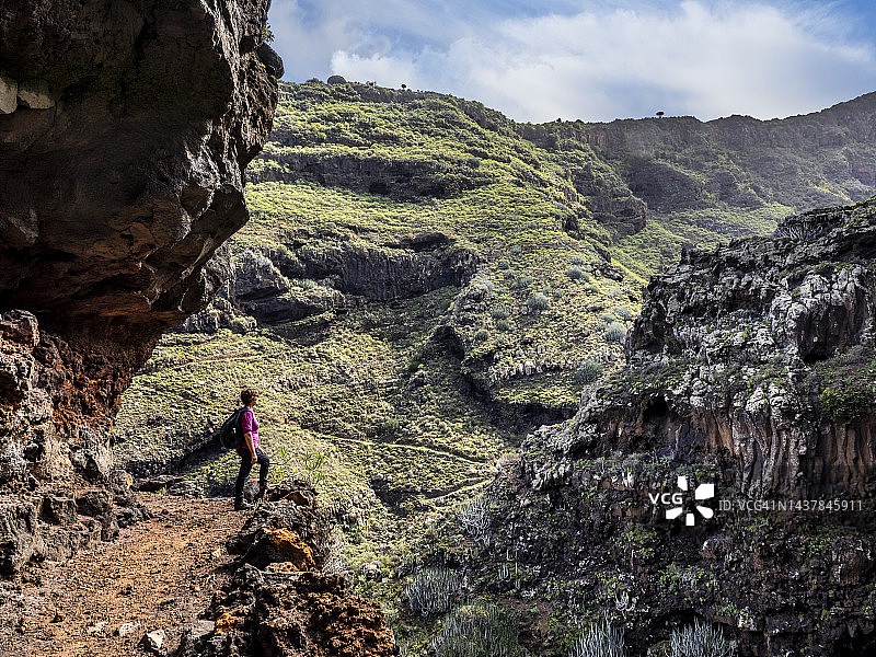 在拉帕尔马加那利岛，一位妇女走在峡谷间的山路上，凝视着风景。图片素材