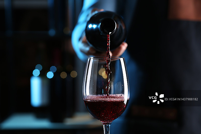 室内特写，调酒师将红酒从酒瓶倒入玻璃杯图片素材