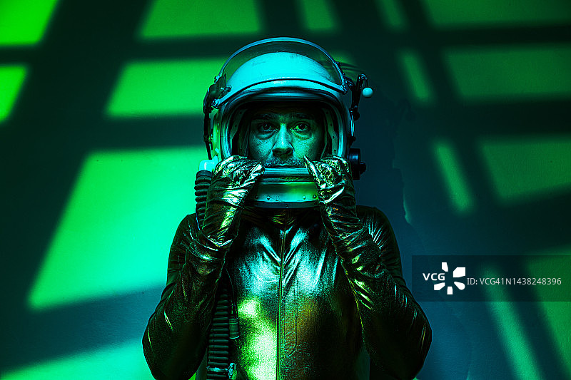 宇航员穿着金色的连体衣和头盔，在绿色的环境中，背景是网格状的光和绿色的阴影。探索，太空，行星，奇怪的和陌生的。图片素材