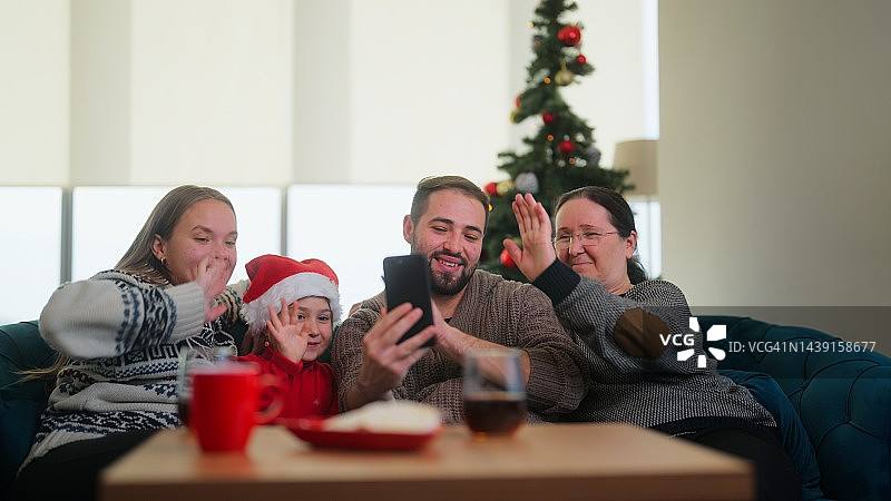 在圣诞节期间，两代人坐在客厅里，通过视频电话与其他家庭成员或朋友联系图片素材