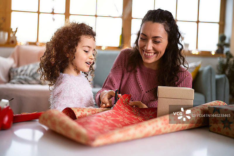 一名妇女用剪刀剪圣诞包装纸，她的女儿在一旁帮助她图片素材