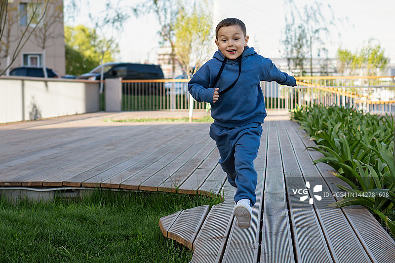 小男孩穿着蓝色运动服在操场上跑步。积极快乐童年，生活方式。户外活动，产品，游戏，儿童服装图片素材
