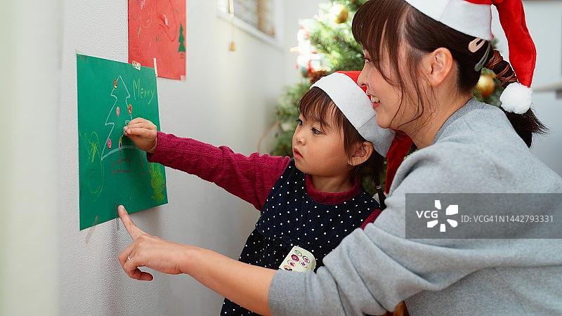 母亲和她学龄前的小女儿用自制的圣诞装饰品装饰他们的家图片素材