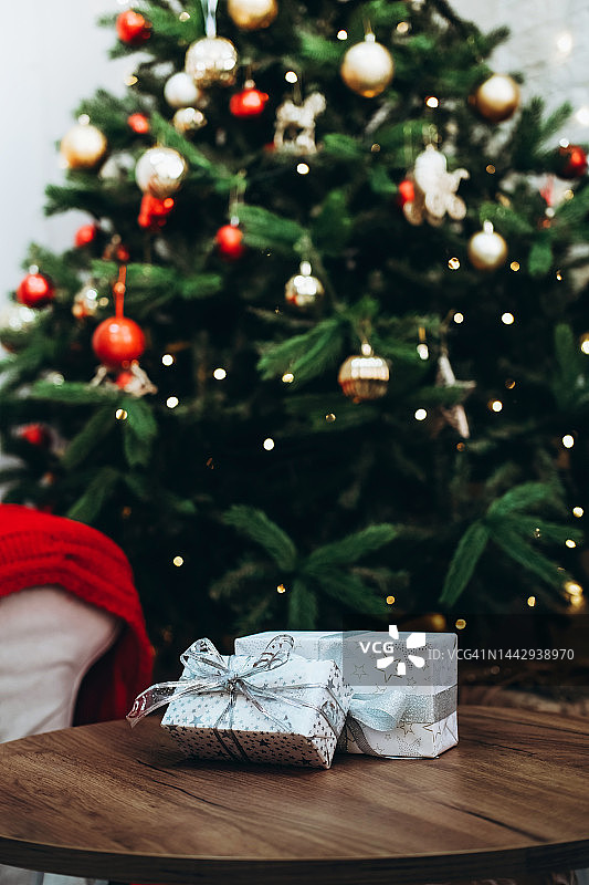 白色礼品盒与银色蝴蝶结附近的圣诞树与led花环。图片素材