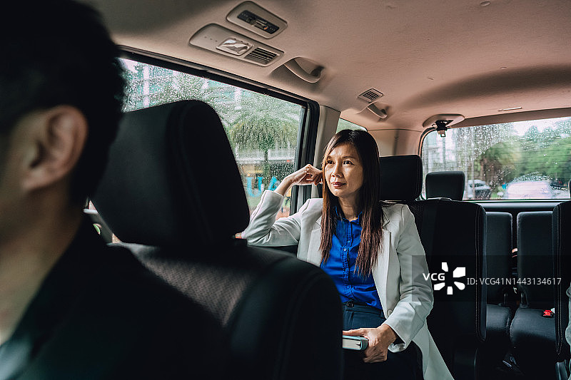 一位亚洲女商人坐在公司MPV汽车的后座上向窗外看图片素材