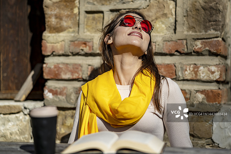 一位妇女在自家门前看书，享受着秋日的阳光。图片素材