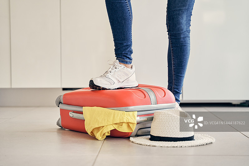 特写镜头:一个无法辨认的女人用脚关上装满衣服的行李箱，试图把它关上，然后去度假。图片素材