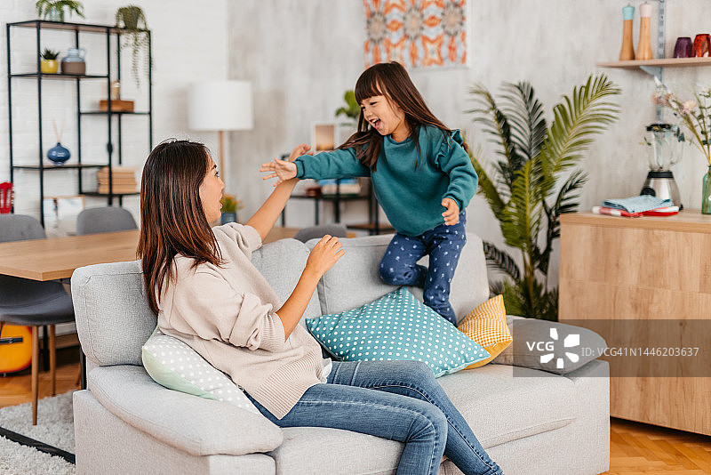 年轻的母亲和女儿在客厅的沙发上玩耍图片素材