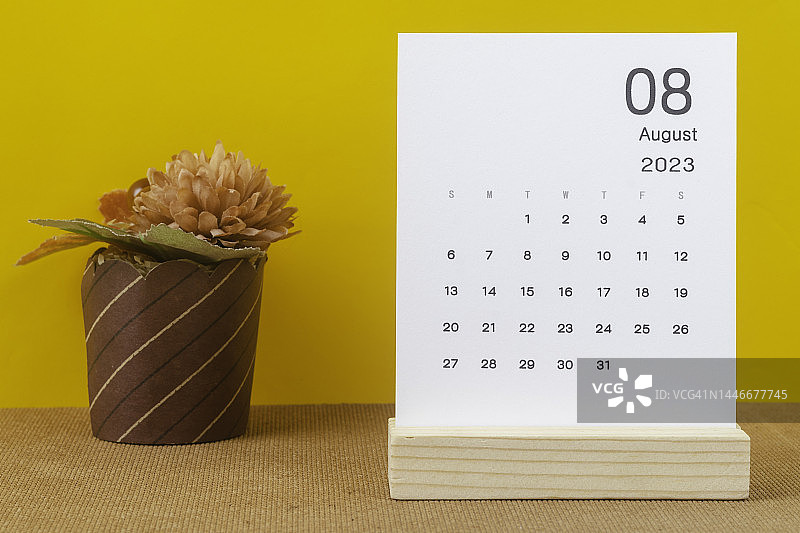 2023日历台:8月是组织者计划和截止日期的月份，黄色纸背景手工制作的花。图片素材