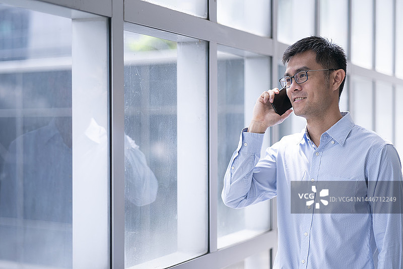 亚洲男性在普通办公室窗口附近使用手机图片素材