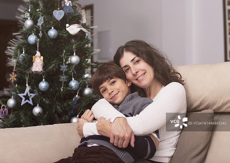 在家的圣诞树旁，妈妈抱着儿子，微笑着看着镜头图片素材