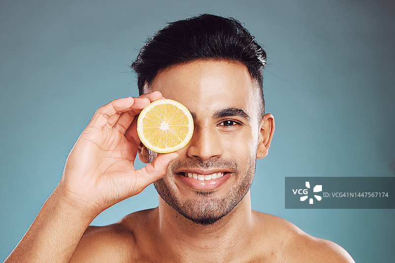 快乐的工作室肖像，男人柠檬护肤美容健康和面部健康的蓝色背景。年轻的快乐模型，美容水果健康的面部皮肤或维生素c与墙背景图片素材