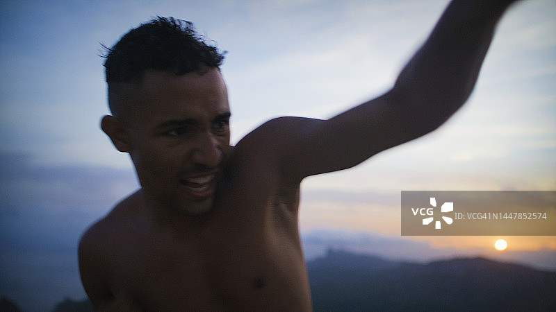 男性肌肉发达的运动员独自在悬崖上训练。练习拳击动作和出拳图片素材