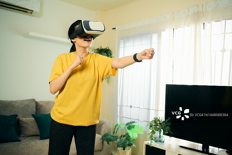 亚洲女性带着VR眼镜在家里的客厅玩虚拟现实游戏图片素材