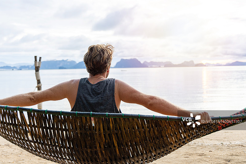 日出时分，男子在海滩上的吊床上放松图片素材