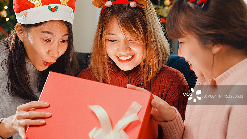 特写一群年轻的亚洲朋友在家里客厅的沙发上打开圣诞礼物。图片素材
