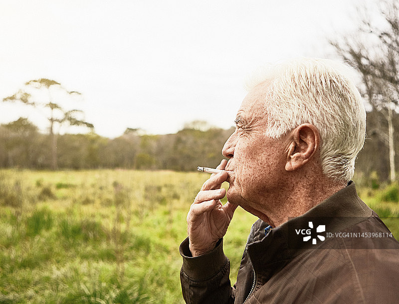 老人站在大自然的户外，看着风景，抽着烟图片素材