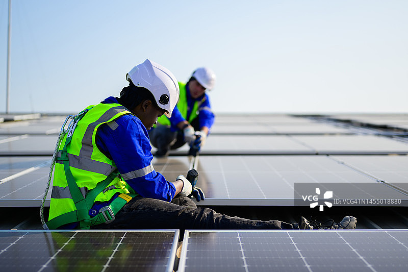 在工厂屋顶安装太阳能电池板的专业技术人员，太阳能电池农场发电厂的工人检查和操作系统，电力和动力的可再生能源，太阳能电池维护概念图片素材