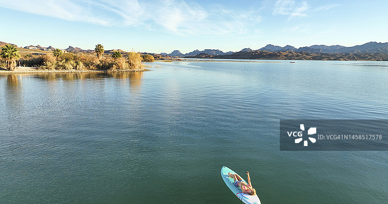 女性桨板选手(SUP)在平静的湖岸放松图片素材