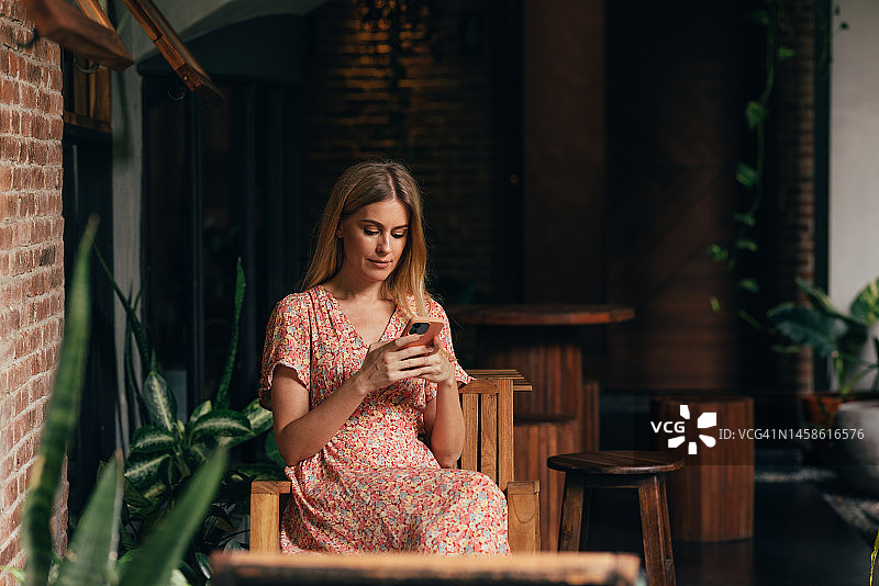 一个快乐的美丽金发女商人坐在咖啡馆里用手机发短信图片素材