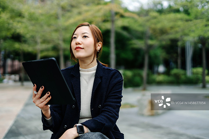 坚定而自信的年轻亚洲女商人，坐在城市办公园区的长椅上，在工作时间用平板电脑工作。忙碌的生意图片素材