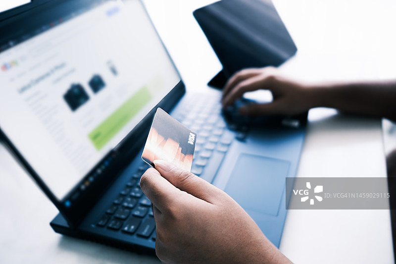 亚洲男性用笔记本电脑上网购物，在家输入信用卡信息进行移动支付。图片素材