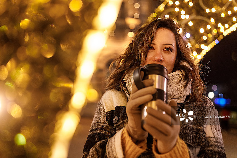 一个年轻的女人在街上等朋友的时候用一杯咖啡暖她的手图片素材