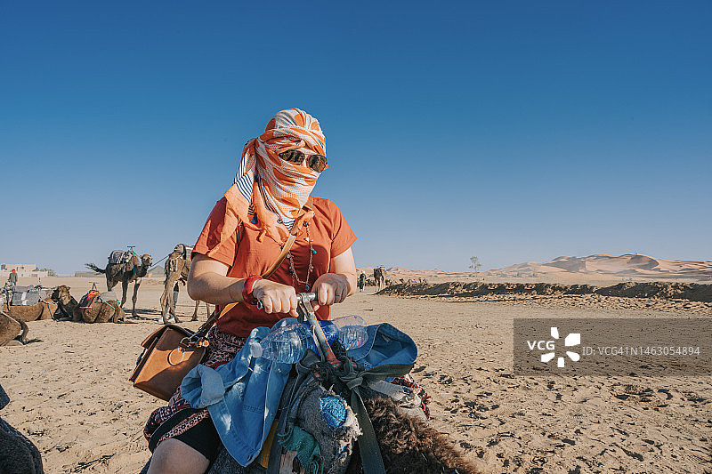 亚洲中国女游客乘坐单峰骆驼火车穿越撒哈拉沙漠摩洛哥图片素材