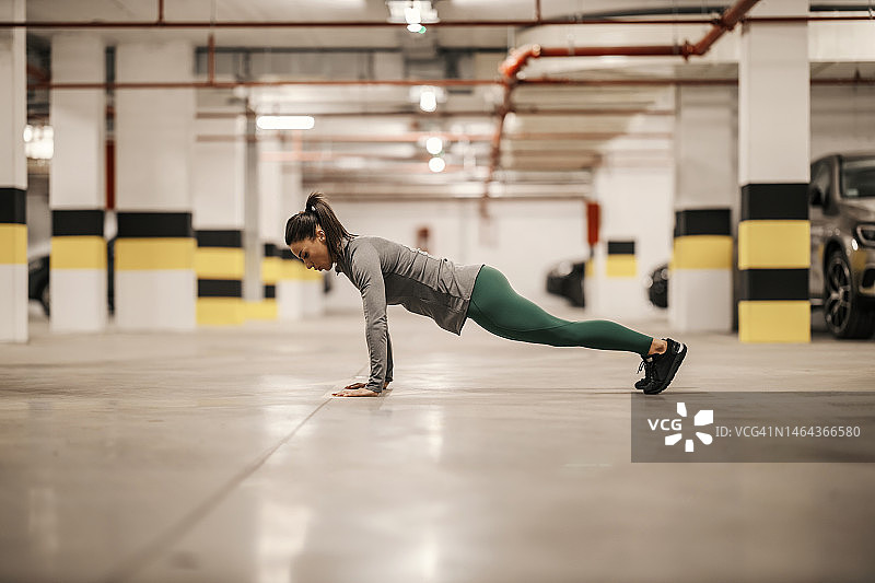 侧面的强烈运动的女人做俯卧撑在地下车库。图片素材
