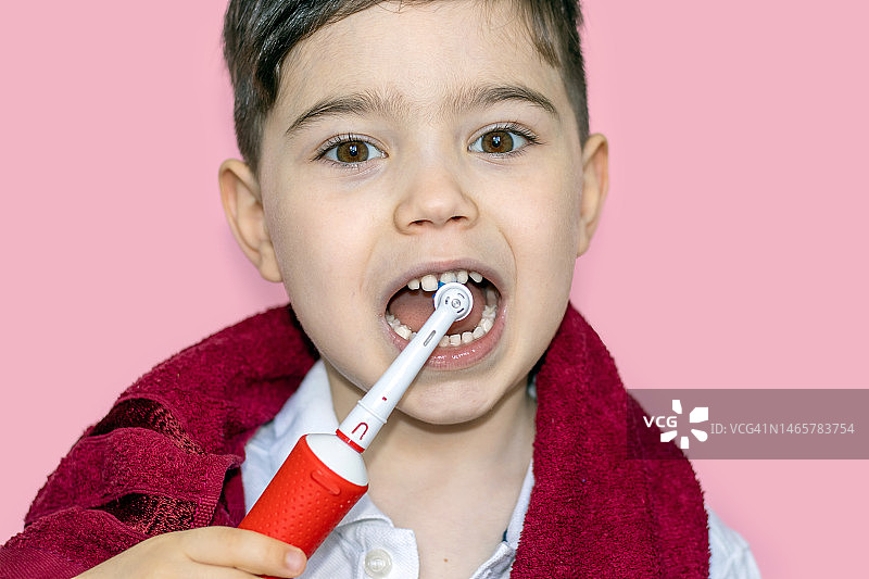 小孩，小孩，婴儿，在牙医柜里，戴着手术手套，用镜子嘴检查牙齿。学龄前男孩在粉红色浴袍上用电动牙刷清洁图片素材