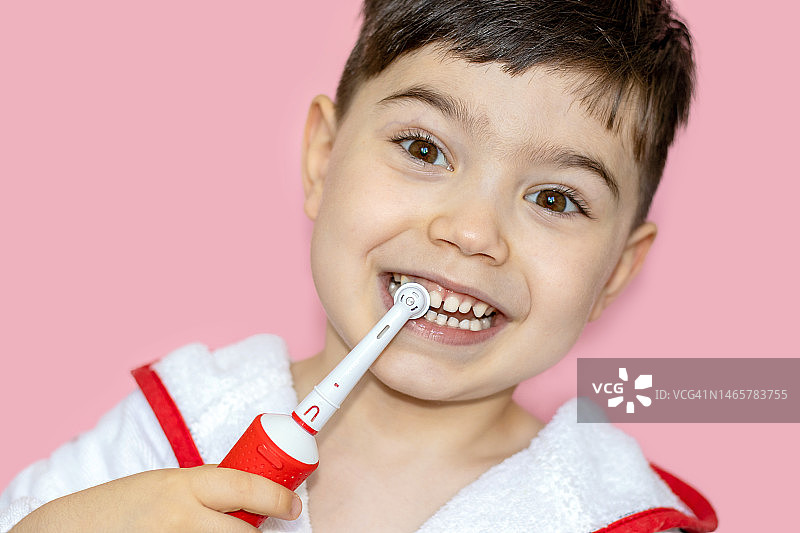 小孩，小孩，婴儿，在牙医柜里，戴着手术手套，用镜子嘴检查牙齿。学龄前男孩在粉红色浴袍上用电动牙刷清洁图片素材