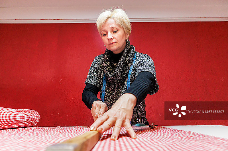 在裁缝店，一名妇女正在用剪刀和尺子准备新衣服。图片素材