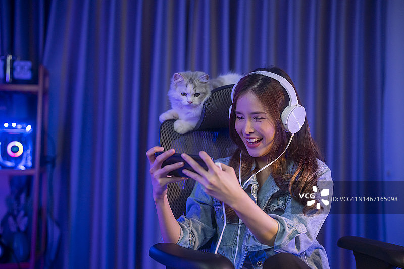 这位年轻的亚洲女孩游戏玩家戴着耳机，用智能手机在线玩视频游戏图片素材