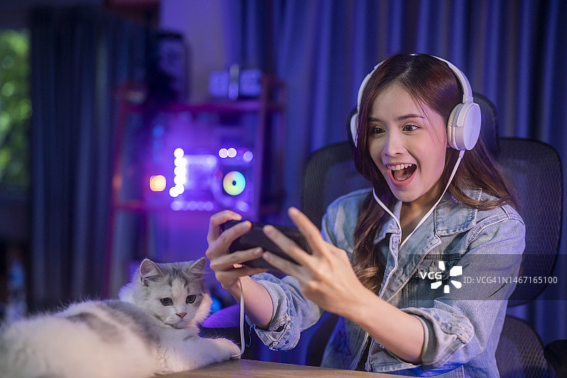 一个快乐的亚洲女孩戴着耳机，用智能手机玩网络游戏图片素材