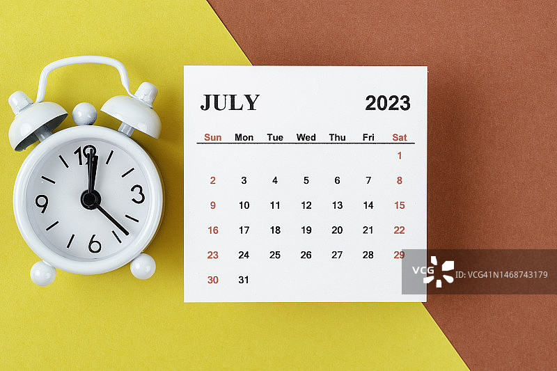 日历桌2023:7月是组织者计划和截止日期的月份，在双色纸背景上有一个闹钟。图片素材