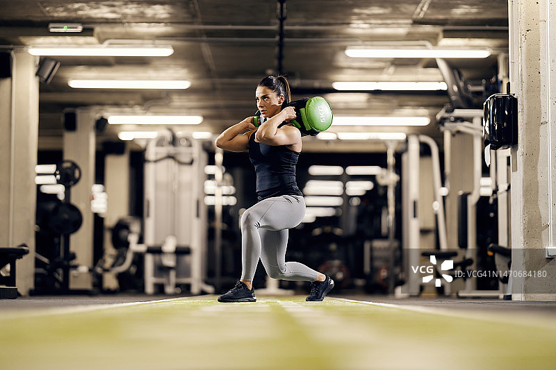 在健身房里，一位女健身运动员正扛着重物做弓步。图片素材