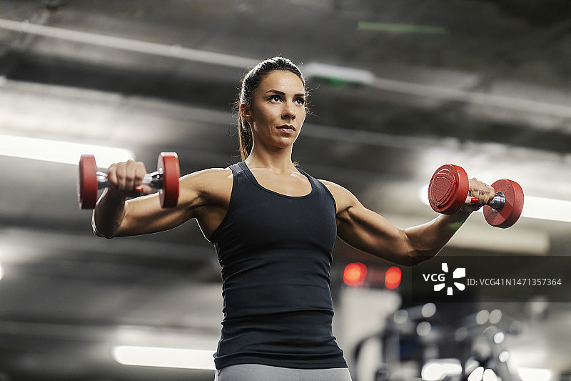 一个肌肉发达的女运动员在健身房举哑铃的低角度视图。图片素材
