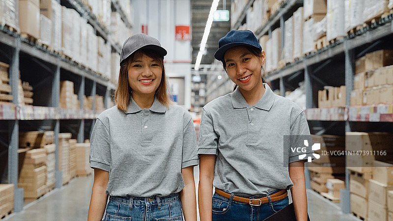 一群年轻的亚洲女工看着相机和手持数码平板电脑的零售仓库。商务仓储在线。图片素材