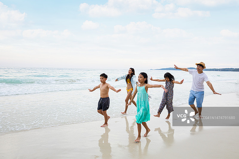 假日，快乐的亚洲家庭一起在海滩上蹦蹦跳跳。快乐家庭旅游度假概念。图片素材