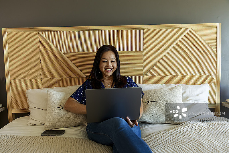 快乐的女人使用笔记本电脑，而坐在床上度假屋图片素材